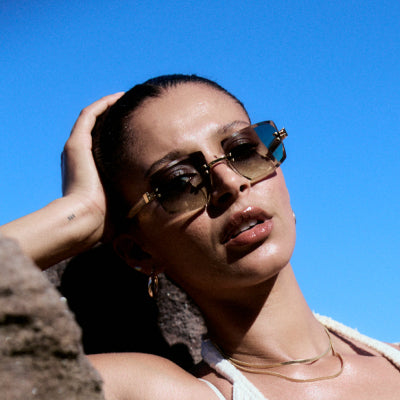 Woman with sleek hair against blue sky wearing rimless angular sunglasses with gradient lenses